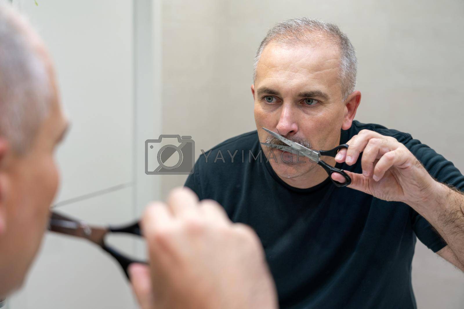 Royalty free image of Middle-aged handsome man using scissors to cut his mustache by Mariakray