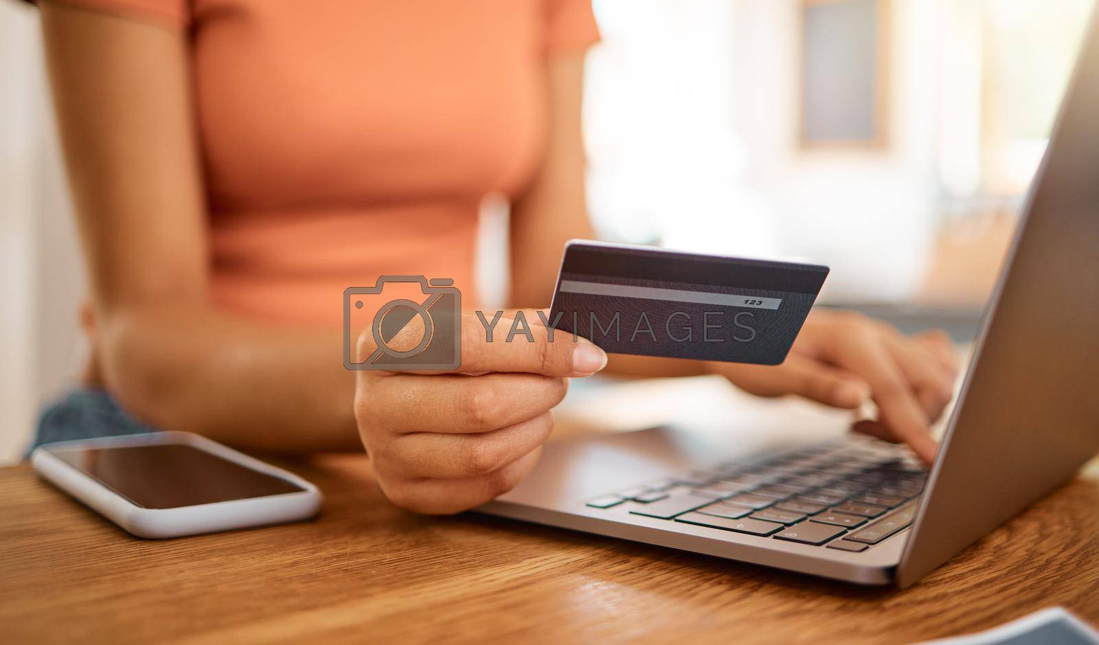 Royalty free image of Businesswoman using a credit card and laptop while working from home. Business professional making an online payment holding a debit card and working on a laptop at home by YuriArcurs