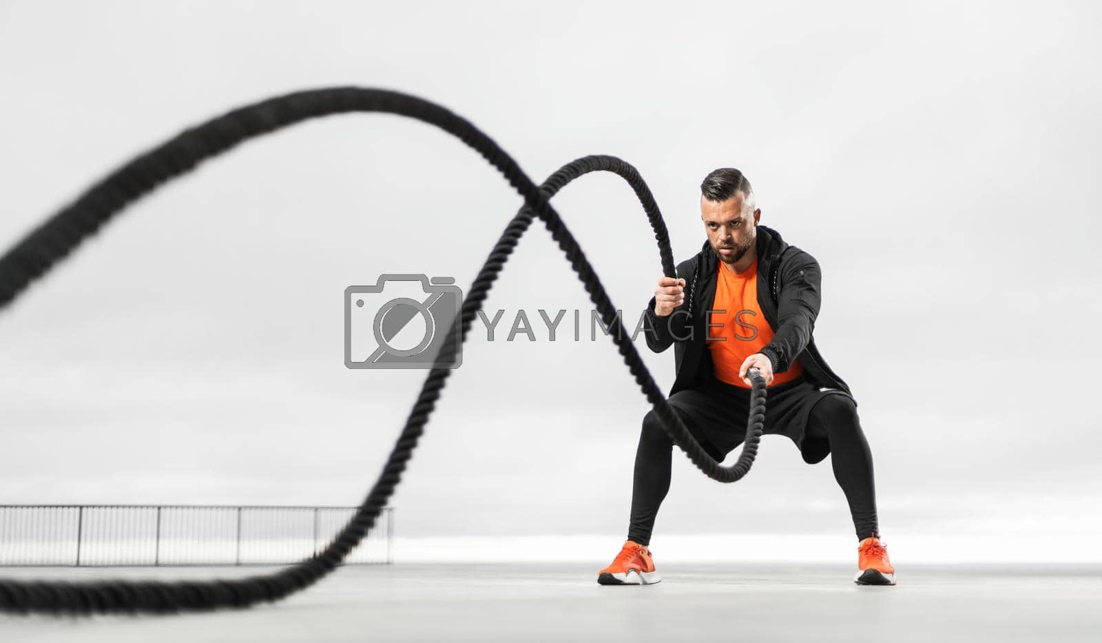 Royalty free image of Fat burning battle rope workout. Athletic man doing sports exercises on the ocean beach by MikeOrlov