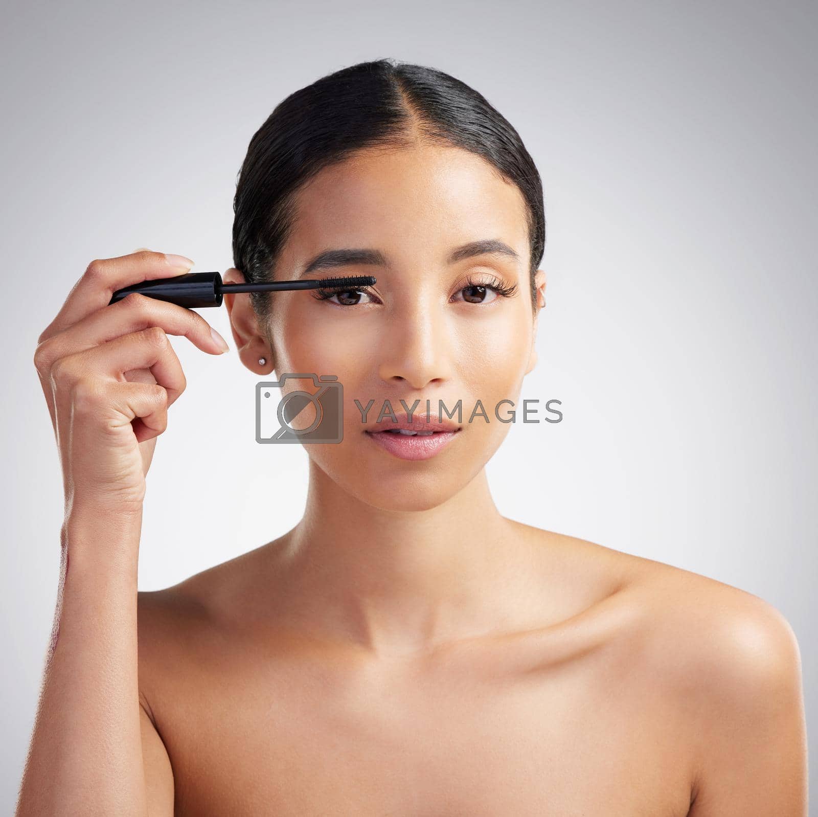 Royalty free image of Studio portrait of a beautiful young mixed race woman with glowing skin posing against grey copyspace background. Hispanic woman with natural looking eyelash extensions applying mascara by YuriArcurs