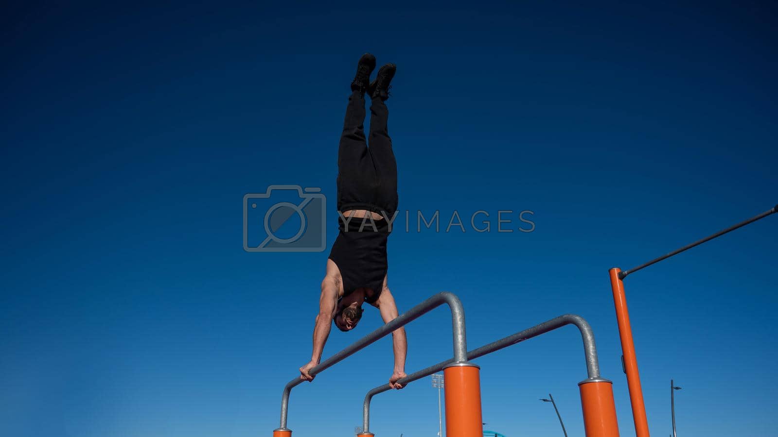 Royalty free image of Shirtless man doing handstand on parallel bars at sports ground. by mrwed54