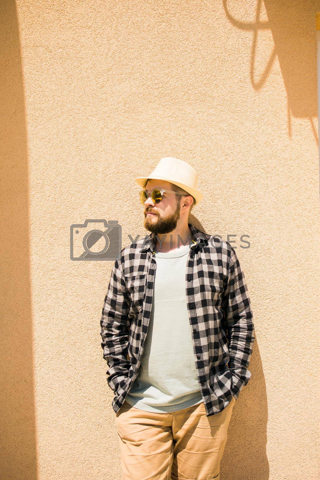 Royalty free image of Fashion millennial stylish man posing on streets of european city. Bearded handsome hipster man posing near wall with hard shadows on hot noonday - summer vacations and holiday concept by Satura86
