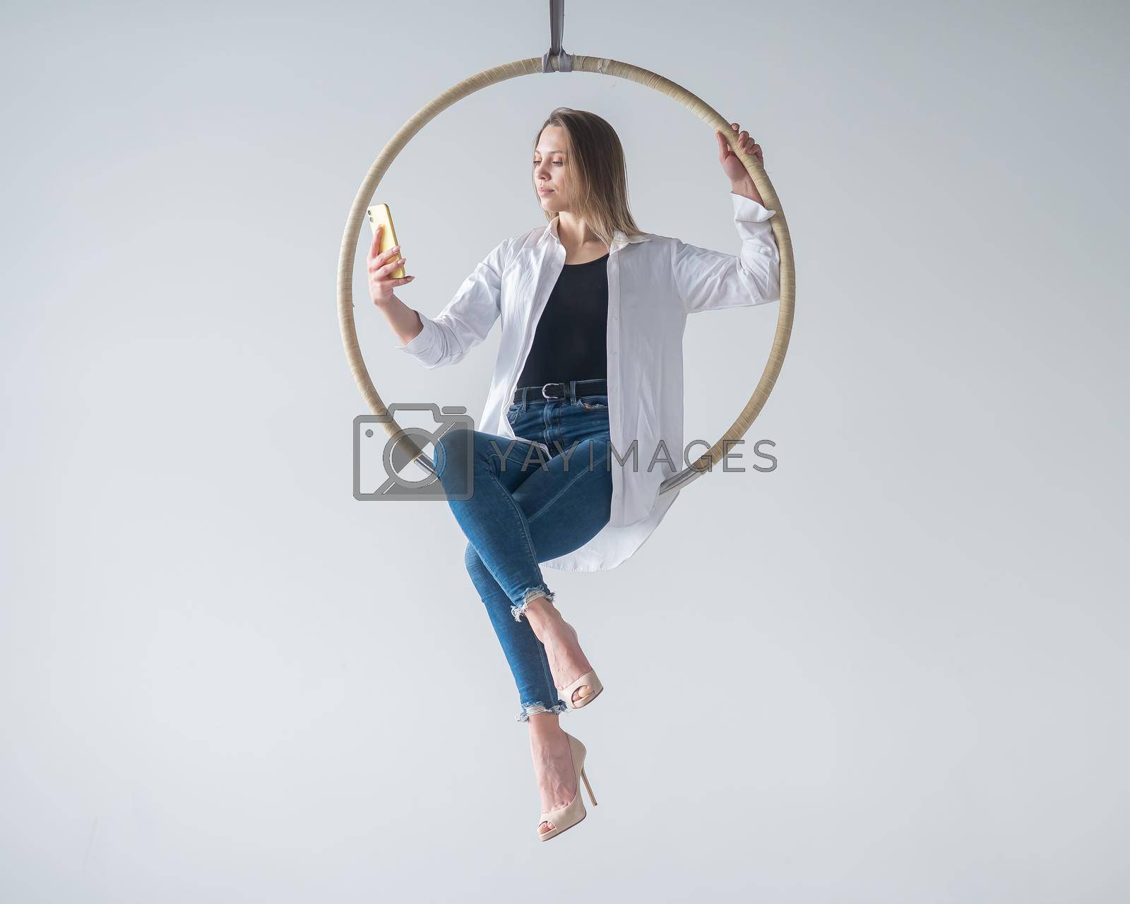 Royalty free image of Caucasian woman gymnast on an aerial hoop takes a selfie on a smartphone. by mrwed54