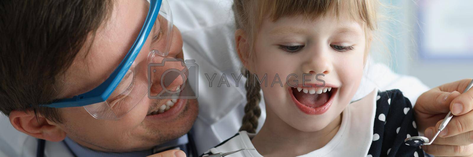 Royalty free image of Man pediatrician check little girls health condition using special tool for mouth by kuprevich