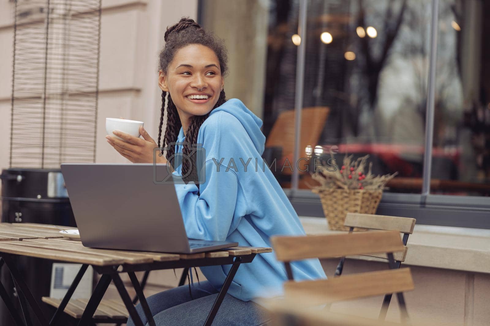 Royalty free image of Attractive young mixed-race happy stylish woman holding coffee and laughing. Cafe terrace. by Yaroslav_astakhov