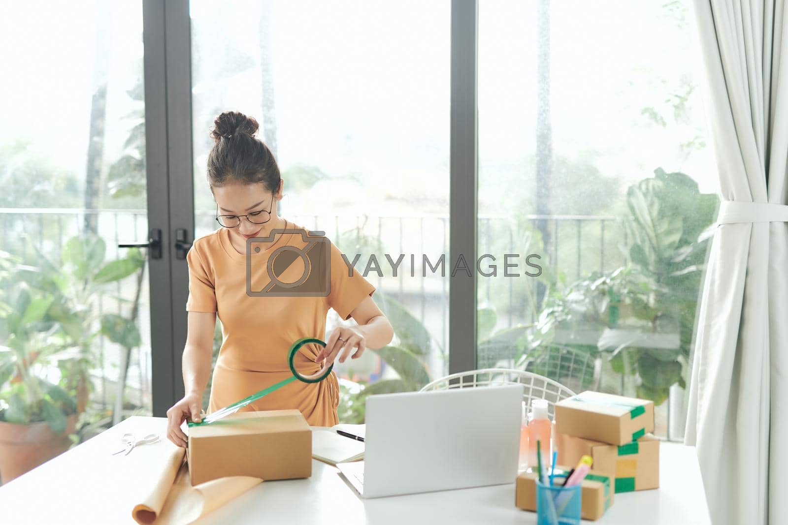 Royalty free image of Smiley Woman Packaging Using Tape Dispenser A woman is preparing a product box to deliver to many customers. by makidotvn