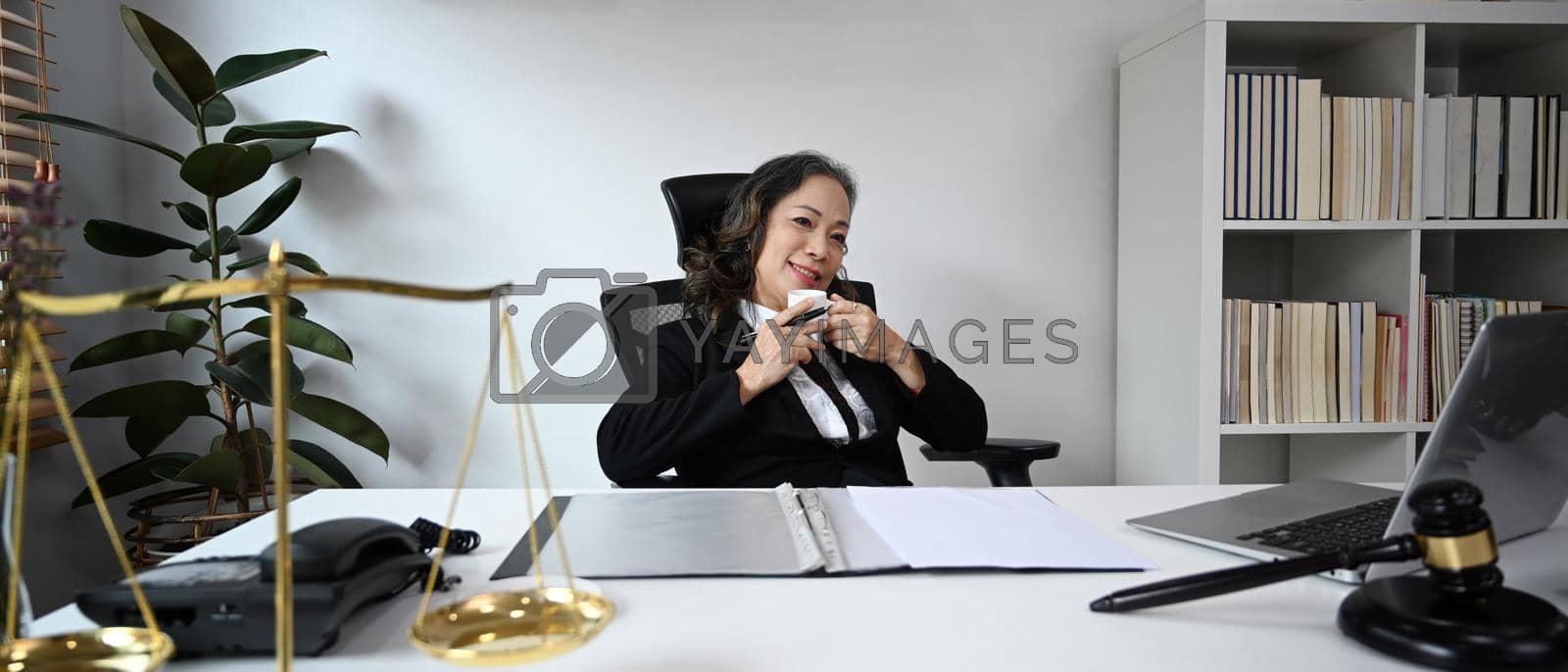 Royalty free image of Mature female lawyer drinking coffee, resting at her personal office by prathanchorruangsak