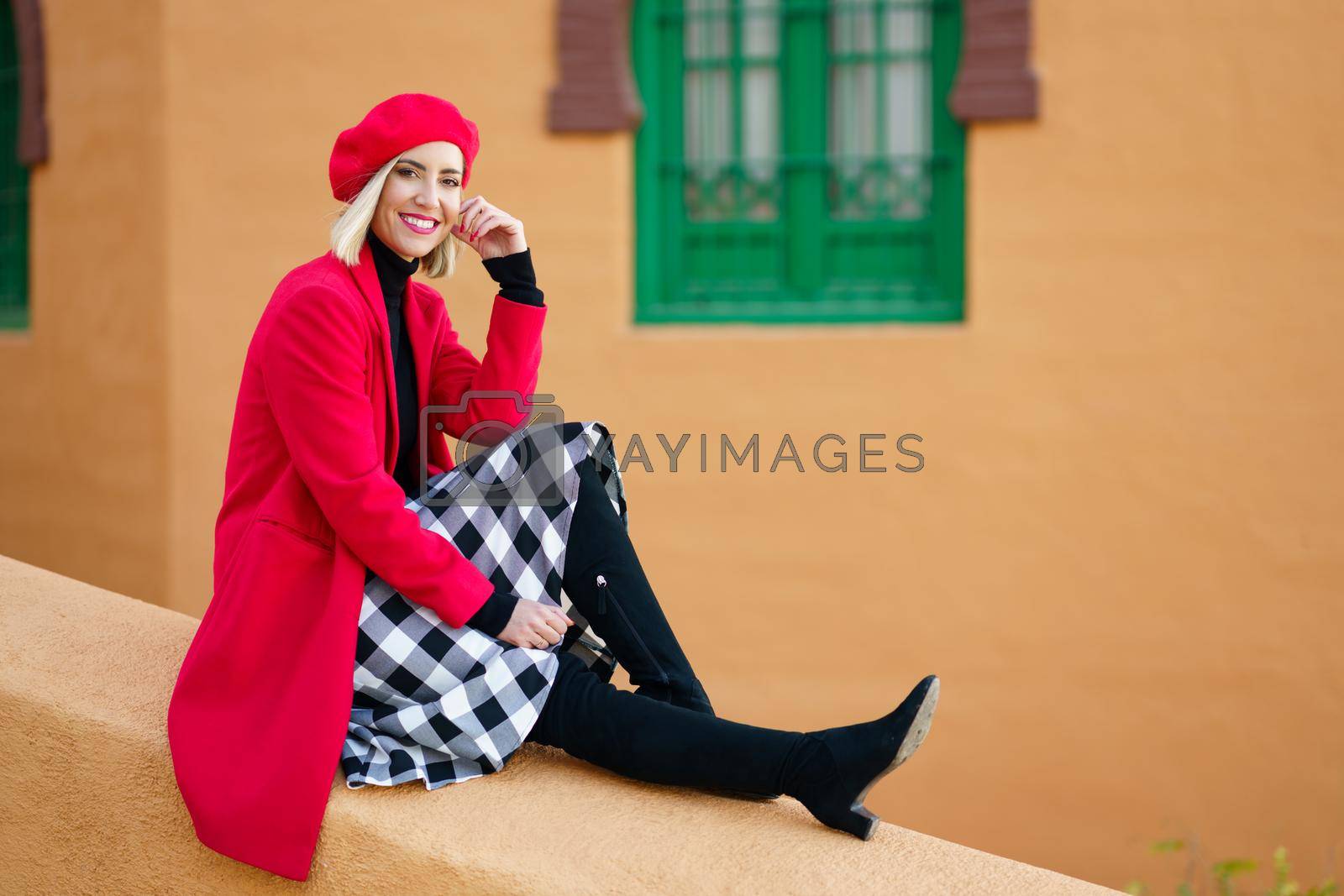 Royalty free image of Stylish happy woman sitting on border near aged colored building by javiindy
