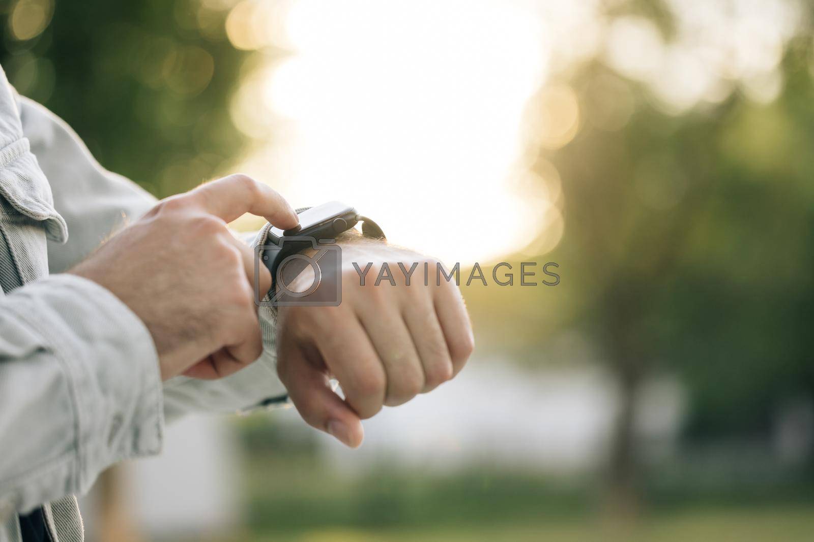 Royalty free image of Close up shot of male's hand uses of wearable smart watch at outdoor in sunset. Smart watch. Smart watch on a man's hand outdoor. Man's hand touching a smartwatch by uflypro