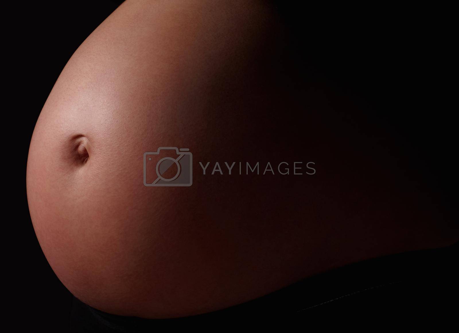 Royalty free image of Detail shot of a pregnant womans belly against black. Belly of a pregnant woman against black background. by YuriArcurs