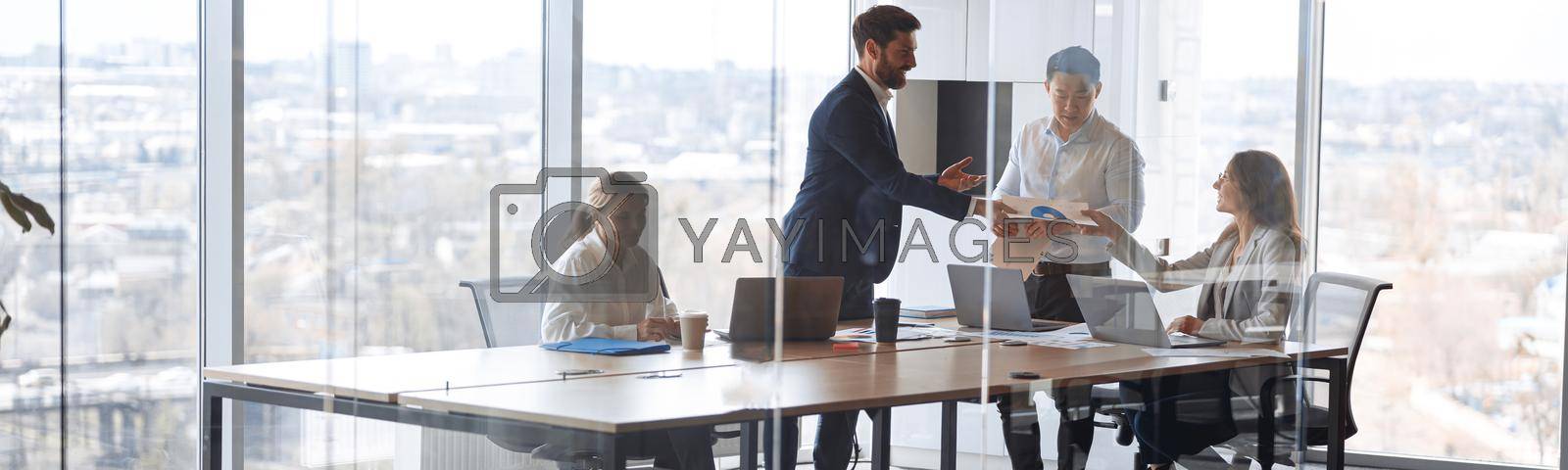 Royalty free image of People standing near table, team of young businessmen working and communicating together in office by Yaroslav_astakhov