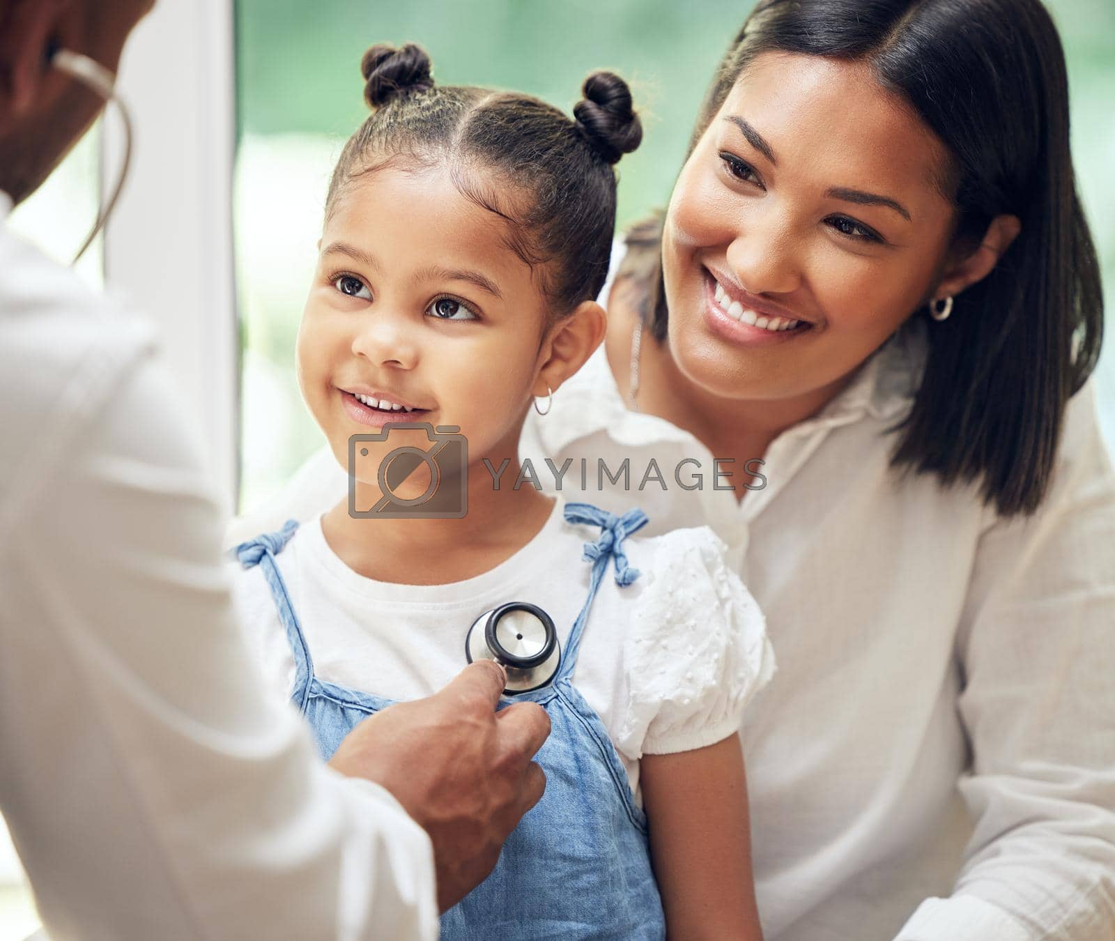 Royalty free image of Doctor examining happy little girl by stethoscope. Child sitting with mother while male paediatrician listen to chest heartbeat. Mom holding daughter during doctor visit by YuriArcurs