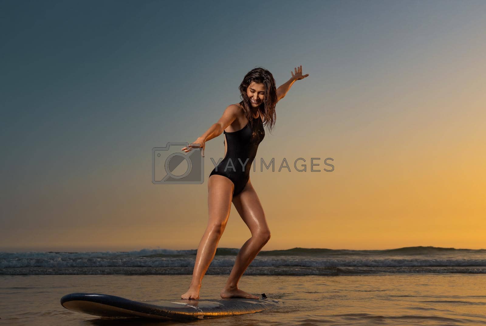 Royalty free image of Surfing training. Surf lessons. Girl with surf board ready to surfing. Woman surfer on the surfboard on a beach at sunset. by MikeOrlov