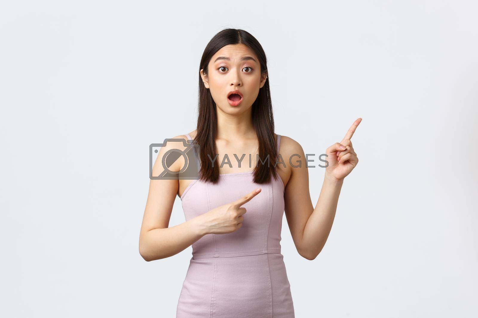 Royalty free image of Luxury women, party and holidays concept. Excited and worried cute asian woman asking question or advice about event, wear evening dress and pointing fingers upper right corner by Benzoix