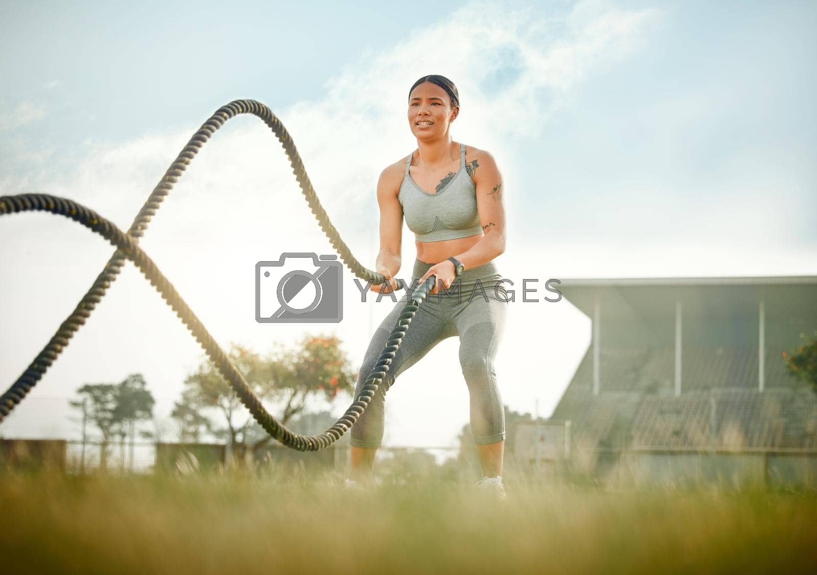 Royalty free image of Pure power. Full length shot of an attractive young female athlete exercising with battle ropes outside. by YuriArcurs