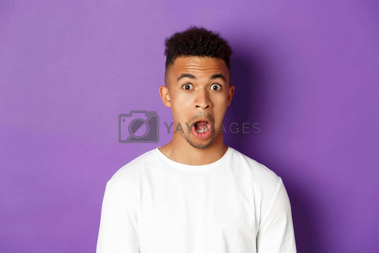 Royalty free image of Close-up of impressed african-american man, drop jaw and stare at something amazed, standing over purple background by Benzoix