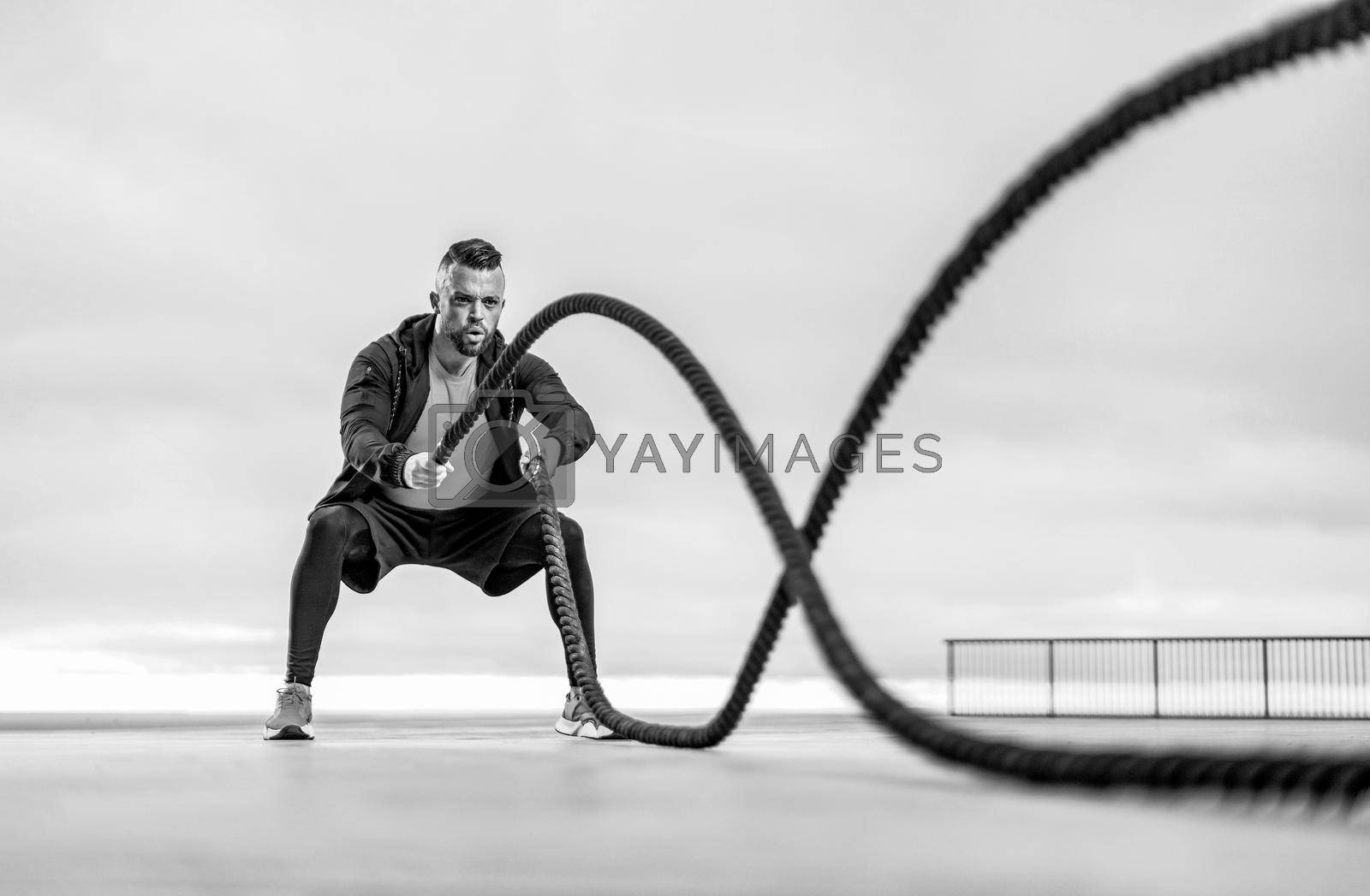 Royalty free image of Athletic man with a battle rope doing sports exercises on the ocean by MikeOrlov