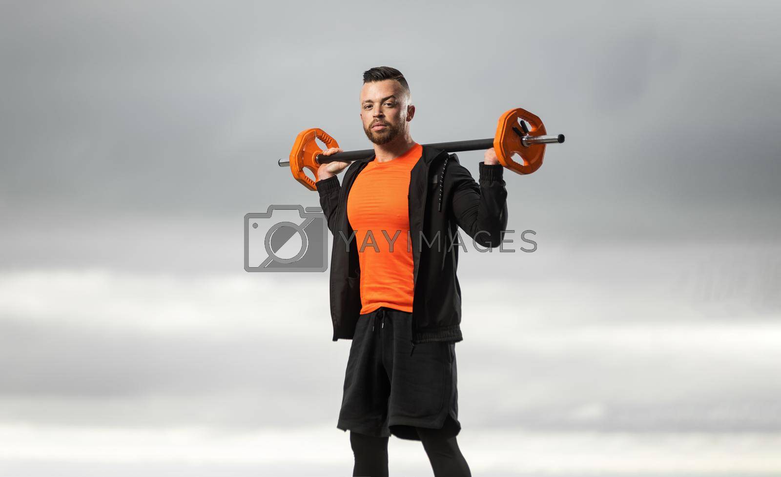 Royalty free image of Man bodybuilder in orange sportswear doing squats using a barbell in a outdoor gym to train legs and back. Powerful fitness workout. by MikeOrlov