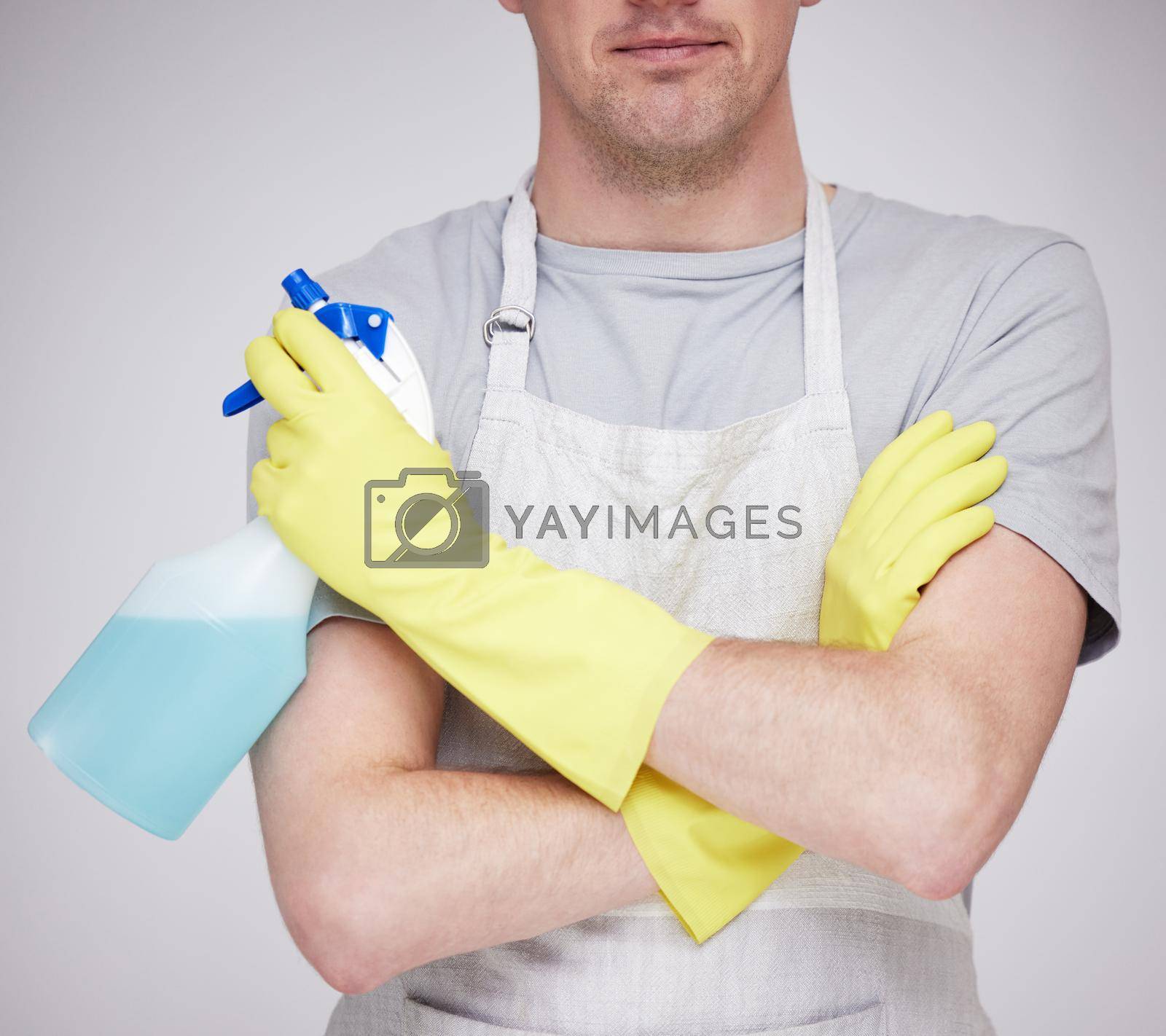 Royalty free image of What needs cleaning today. an unrecognizable man holding a spray bottle with his arms crossed against a grey background. by YuriArcurs