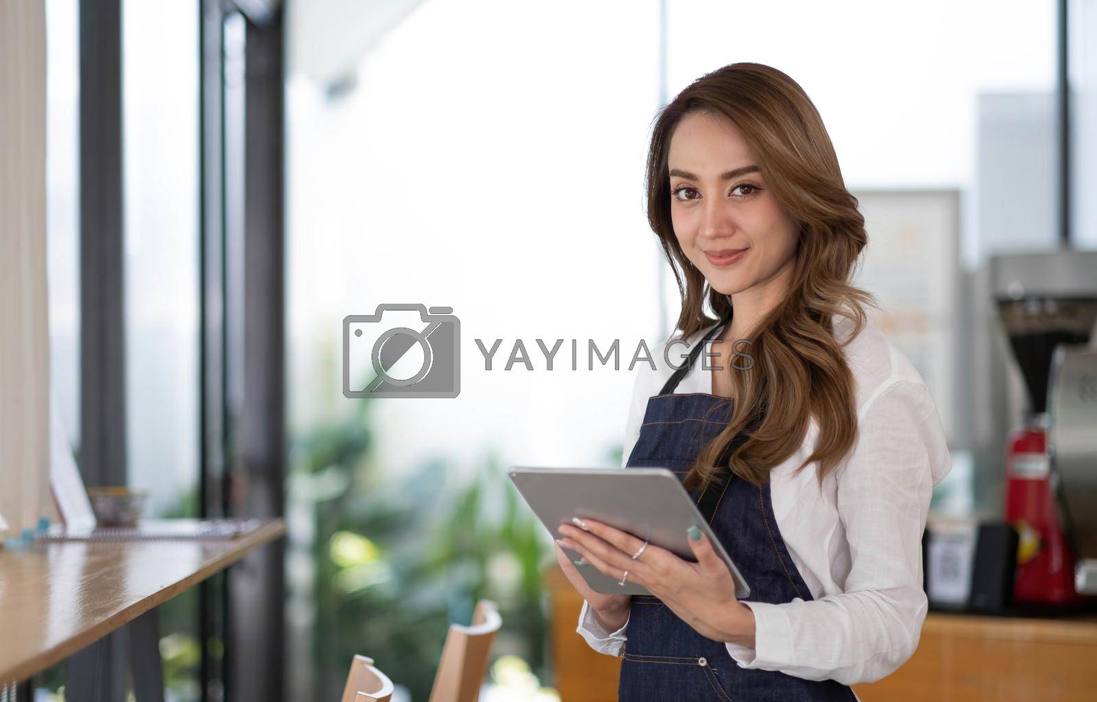 Royalty free image of Startup successful small business owner sme beauty girl stand with tablet smartphone in coffee shop restaurant. Portrait of asian tan woman barista cafe owner. SME entrepreneur seller business concept by wichayada