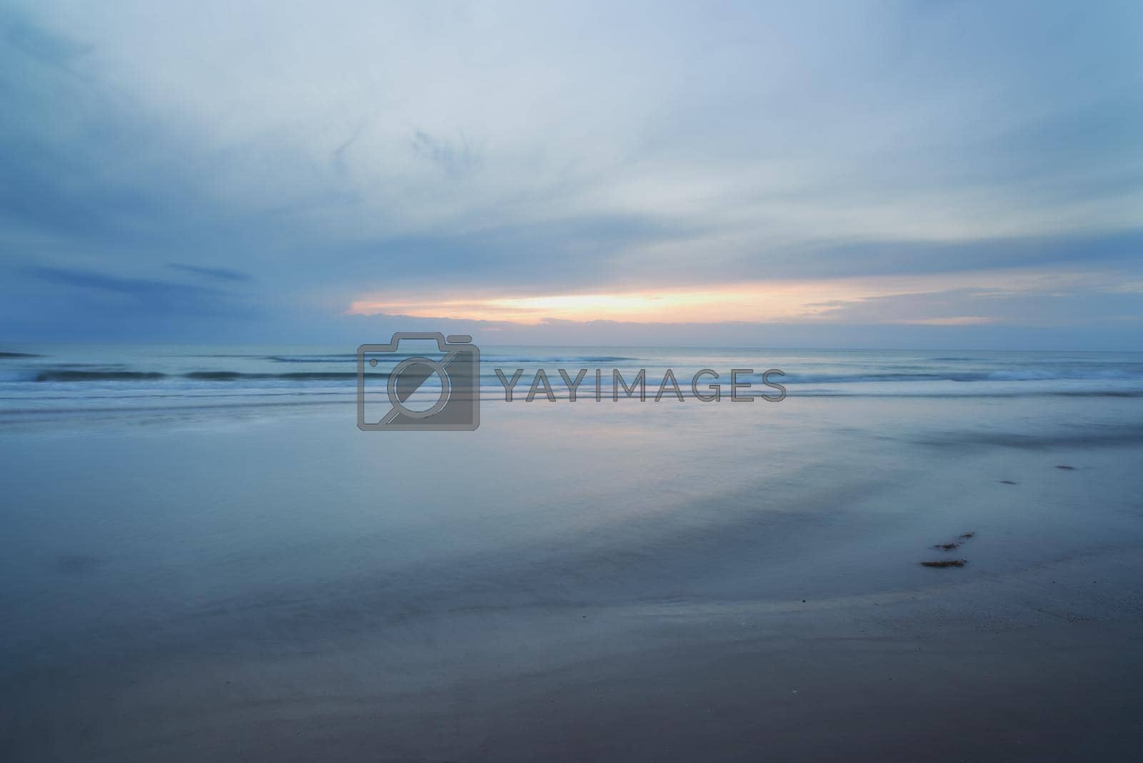 Royalty free image of A beautiful, calm and quiet view of the beach and sunset sky over the horizon with copy space. A peaceful and scenic landscape of endless sandy water of the sea or ocean during low tide at dusk by YuriArcurs