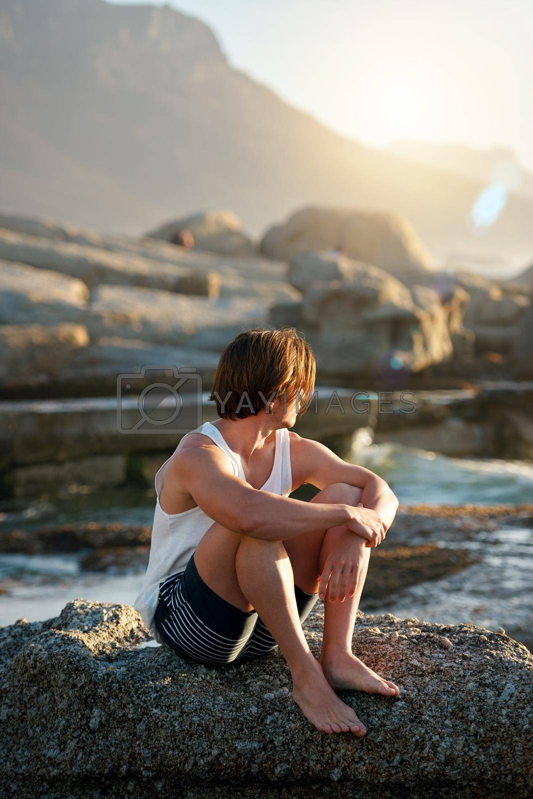 Royalty free image of young man sitting on beach looking at sunset watching ocean contemplating journey by YuriArcurs