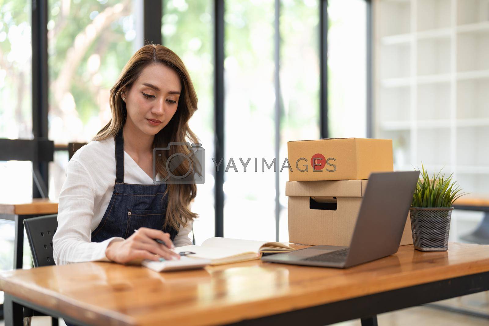 Royalty free image of happy female in apron using calculator and laptop computer in warehouse by nateemee