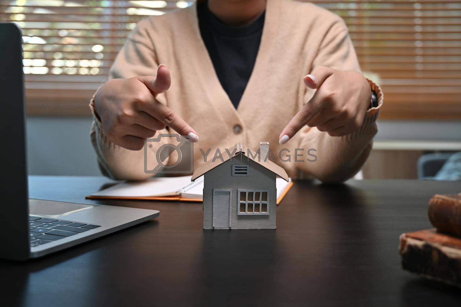 Royalty free image of Young woman pointing to house model on table. Mortgage and real estate investment concept. by prathanchorruangsak
