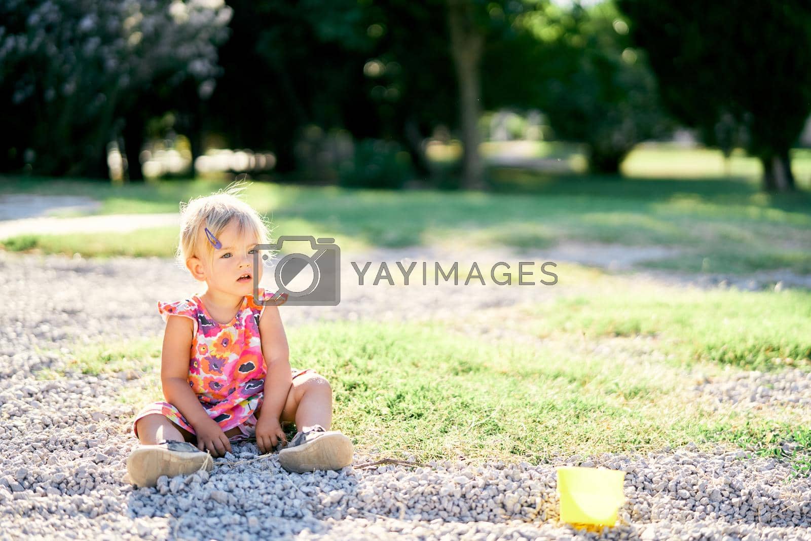Royalty free image of Little girl sits in the park on the pebbles by Nadtochiy