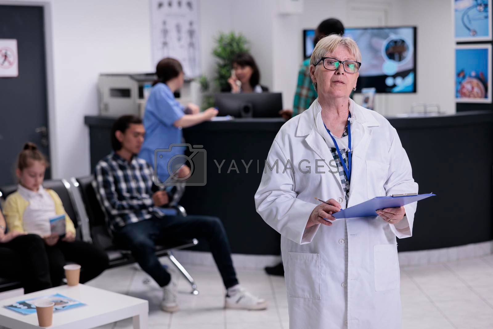 Royalty free image of Portrait of older doctor with stethoscope holding clipboard with patient data in hospital reception by DCStudio