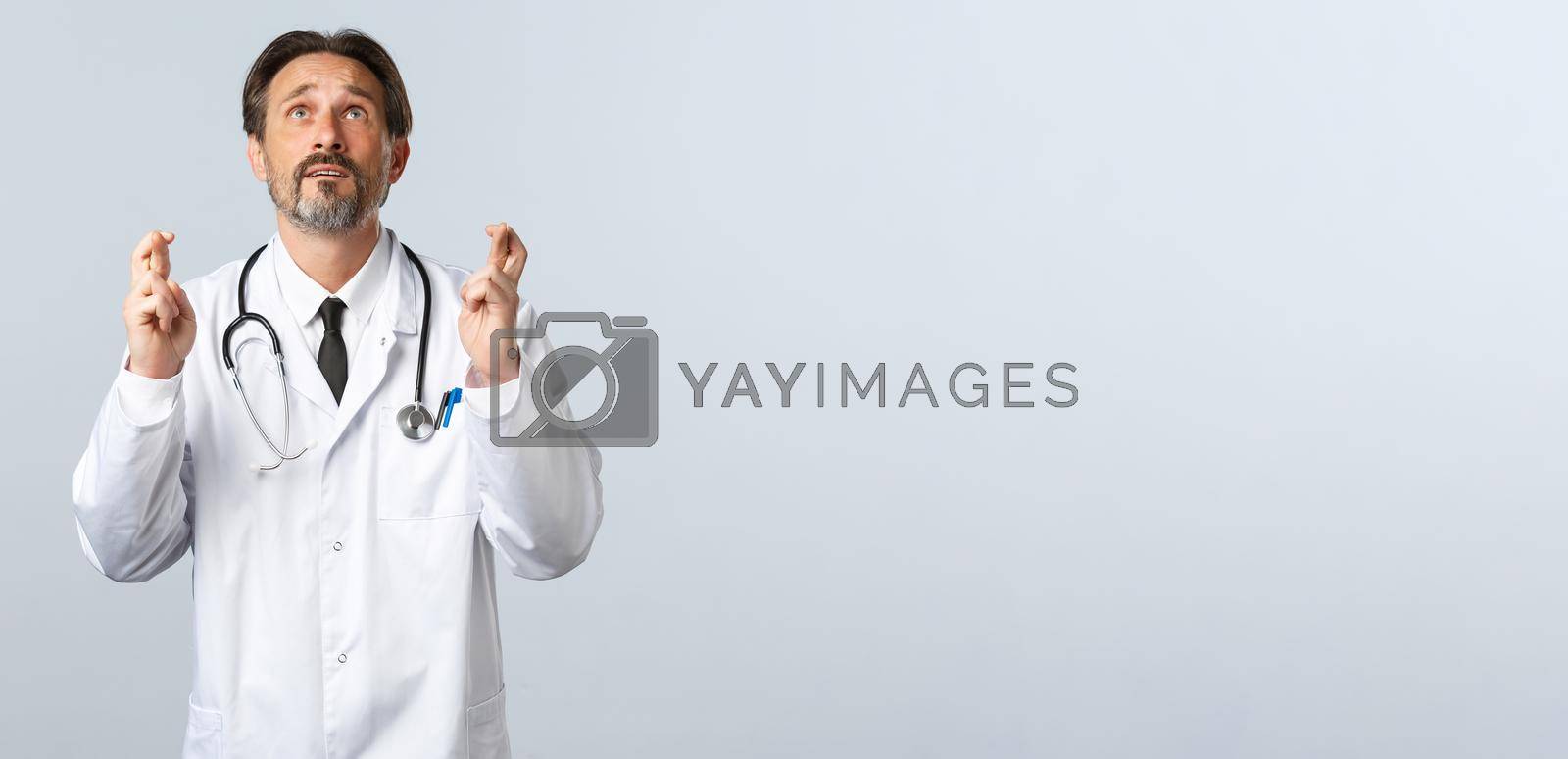 Royalty free image of Covid-19, coronavirus outbreak, healthcare workers and pandemic concept. Hopeful doctor in panic looking up sky, pleading god while cross fingers, make wish, wearing white coat by Benzoix