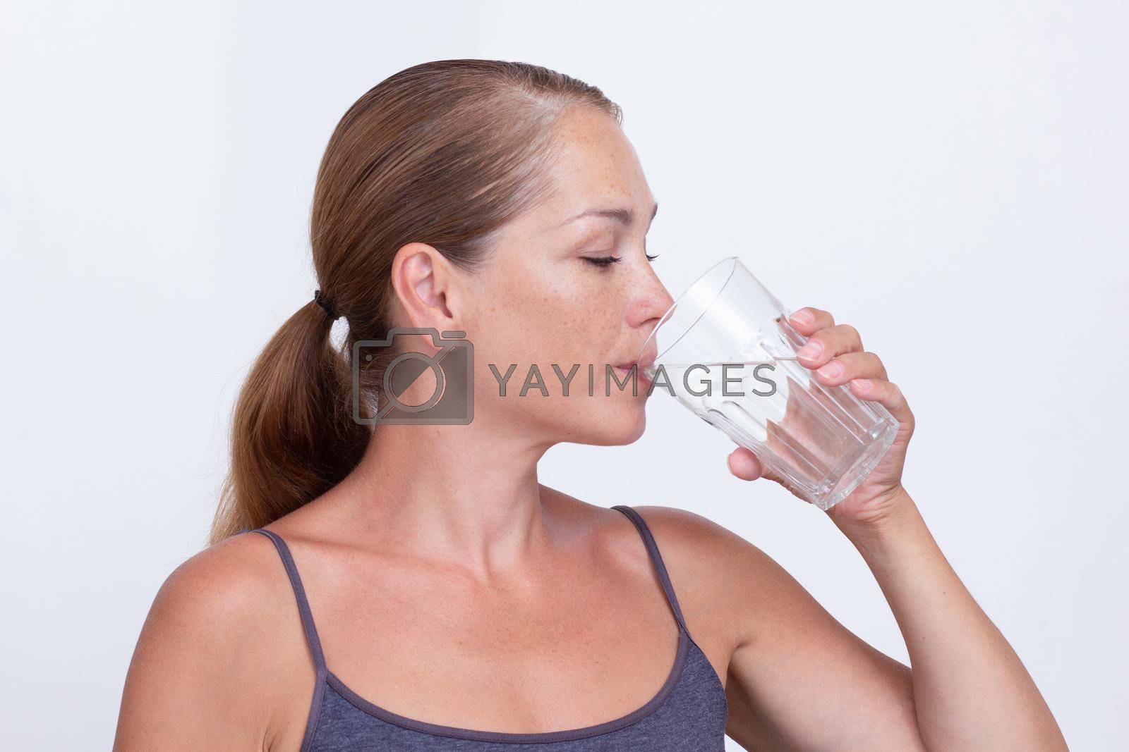 Royalty free image of Woman of 40s holding glass of pure water and drinking by TatianaFoxy