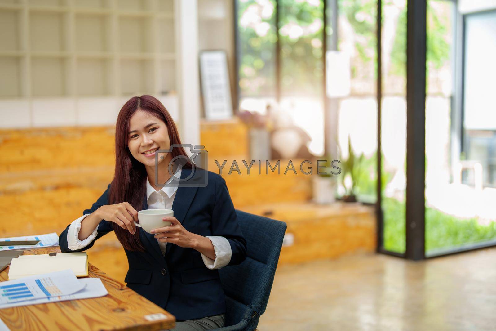 Royalty free image of Asian female worker using computer and budget documents on desk by Manastrong