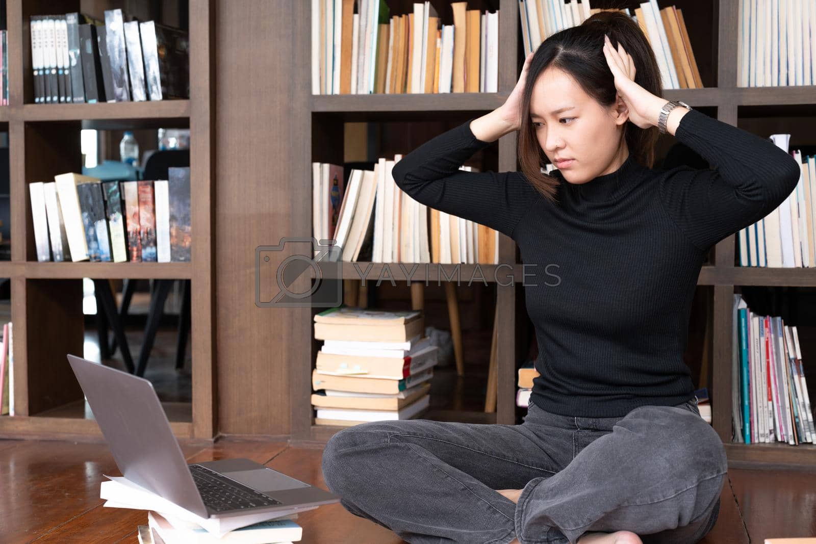 Royalty free image of Unhappy stressed young female student feeling tired preparing for examination, reading books, web surfing information, writing notes in copybook, overworking in modern college library. by nateemee