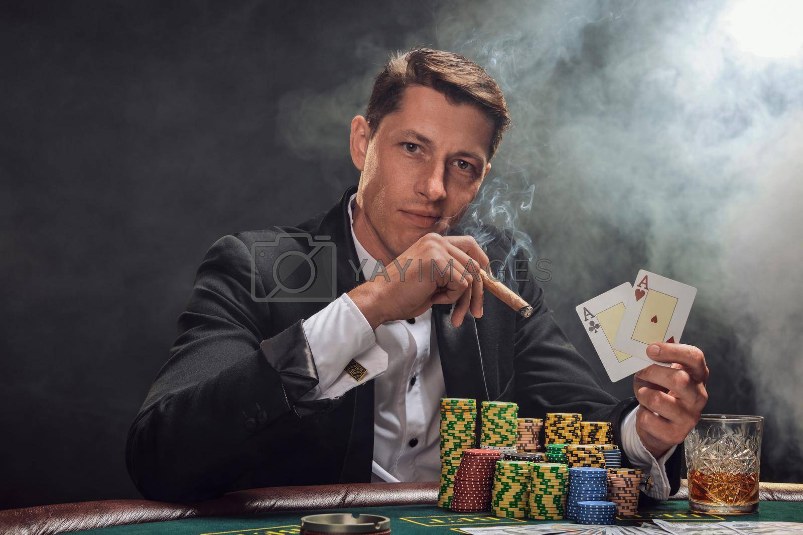 Royalty free image of Handsome emotional man is playing poker sitting at the table in casino against a white spotlight. by nazarovsergey