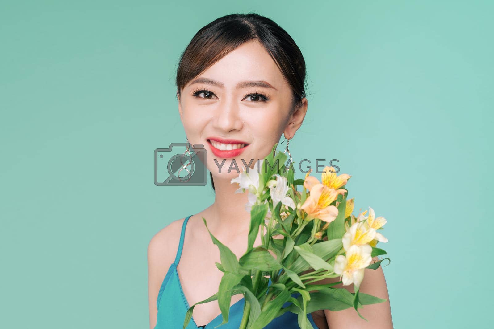 Royalty free image of Attractive Asian woman in blue dress holding bouquet of flowers over blue background by makidotvn