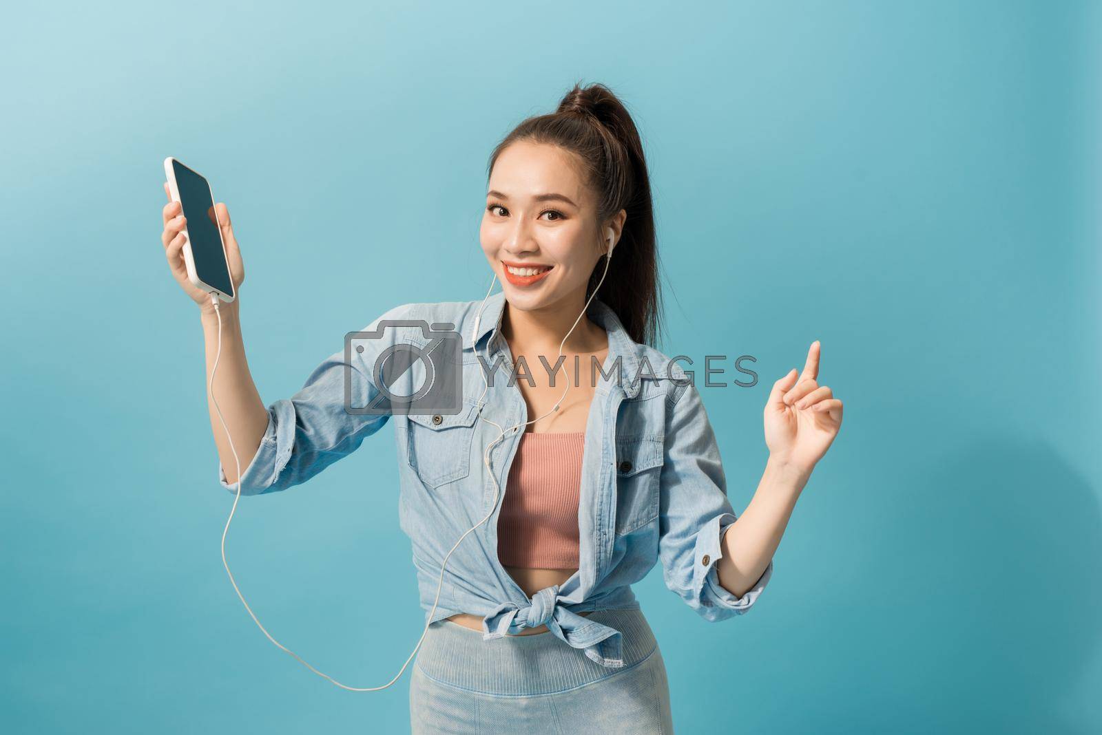 Royalty free image of Cheerful woman in headphones listening to music and dancing isolated over blue background by makidotvn