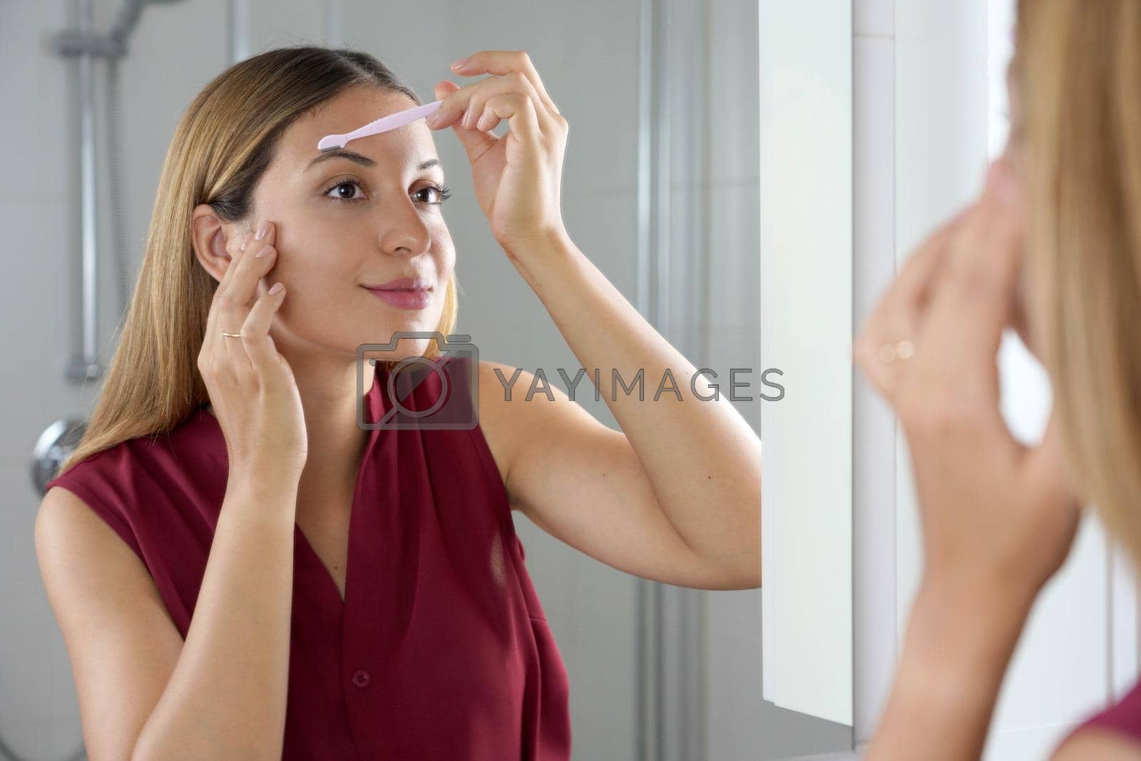 Royalty free image of Hispanic woman shaving her eyebrows with razor in the mirror at home by sergio_monti