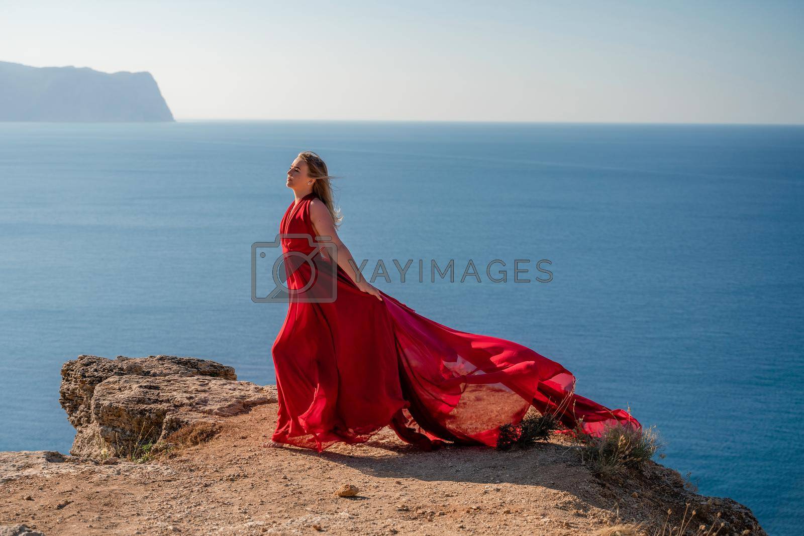 Royalty free image of A woman in a red flying dress fluttering in the wind, against the backdrop of the sea. by Matiunina