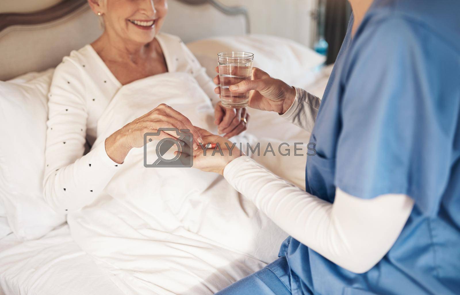 Royalty free image of One daily dose of health coming right up. a nurse giving a senior woman her medication to take with a glass of water in bed. by YuriArcurs