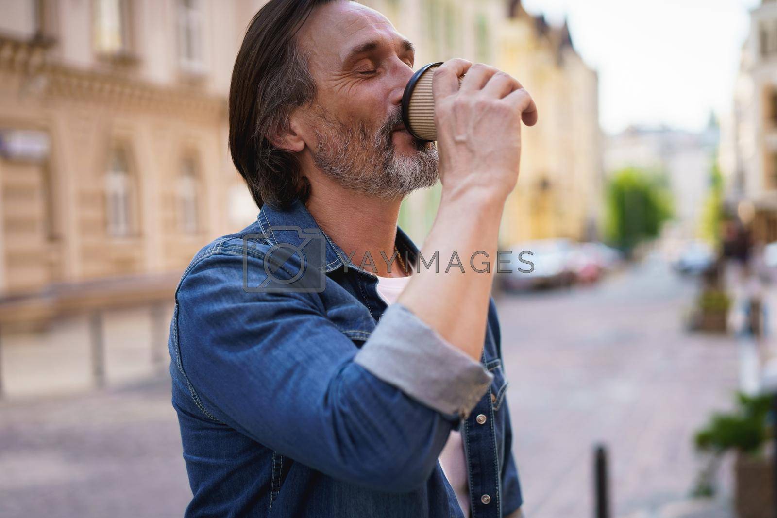 Royalty free image of Enjoying his coffee handsome middle aged man with grey beard standing in the city drink take away coffee from paper cup. Handsome man traveling enjoying free time. Business travel concept by LipikStockMedia