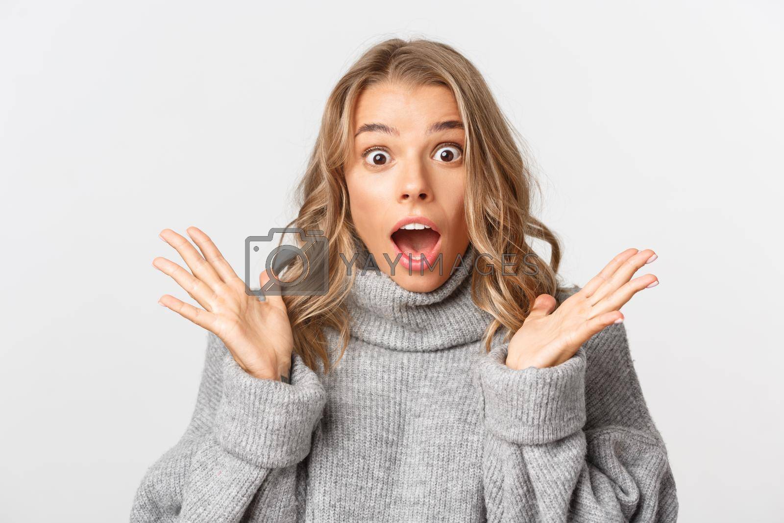 Royalty free image of Close-up of shocked gasping girl in grey sweater, open mouth amazed, standing over white background by Benzoix
