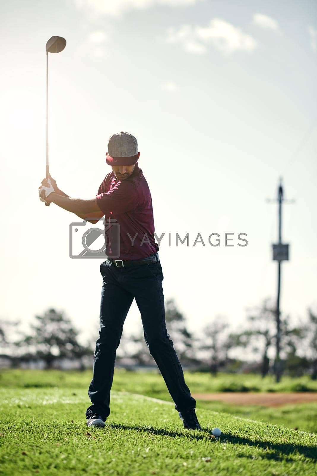 Royalty free image of Pull back and swing. a focused young male golfer about to swing and play a shot with his golf club outside on a course. by YuriArcurs