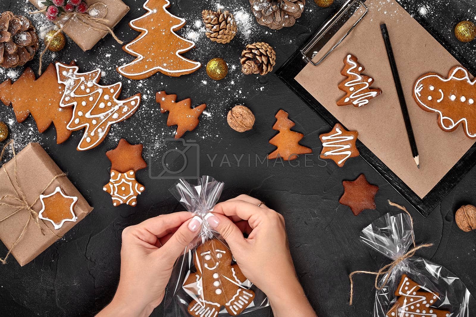 Royalty free image of Christmas gift gingerbread on dark background. Biscuits in festive packaging. Woman is packaging Christmas gingerbread cookies with icing sugar. Top view by nazarovsergey