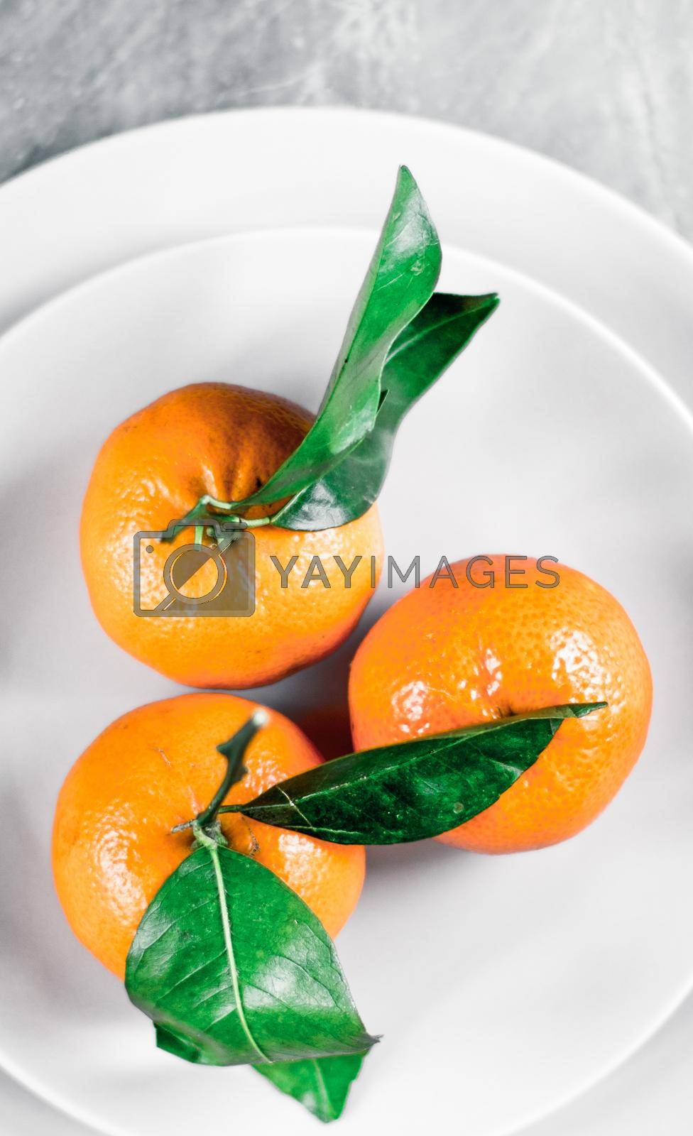 Royalty free image of Tangerines with leaves on plate - citrus fruits and healthy eating flatlay concept by Anneleven