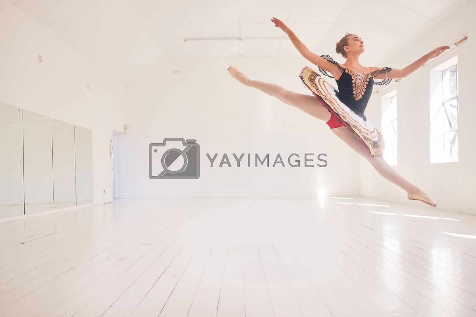 Royalty free image of Jumping or leaping female ballerina, ballet dancer or performer in a traditional tutu dress costume in a studio with copy space background. Young professional performer dancing in ballon mid air pose by YuriArcurs
