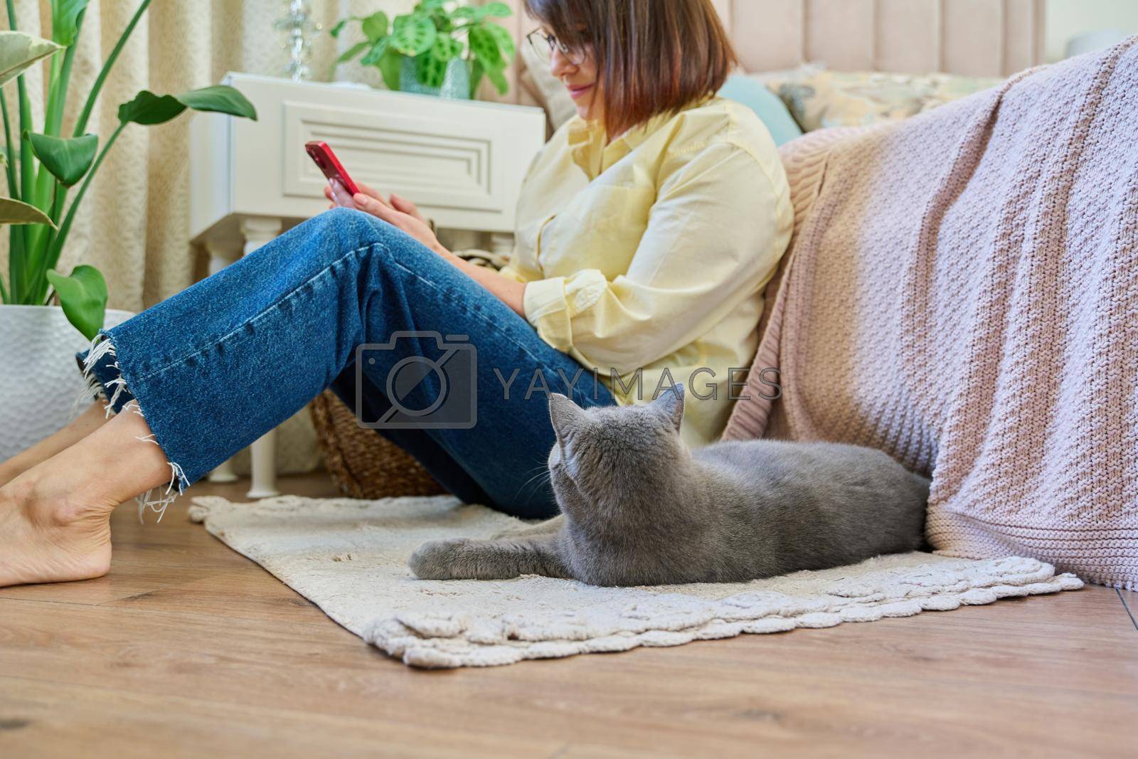 Royalty free image of Female sitting on floor using smartphone, pet cat sleeping near owner by VH-studio