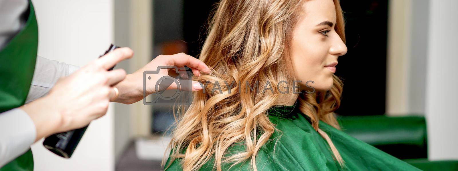 Royalty free image of Hairdresser using hairspray fixing hair by okskukuruza