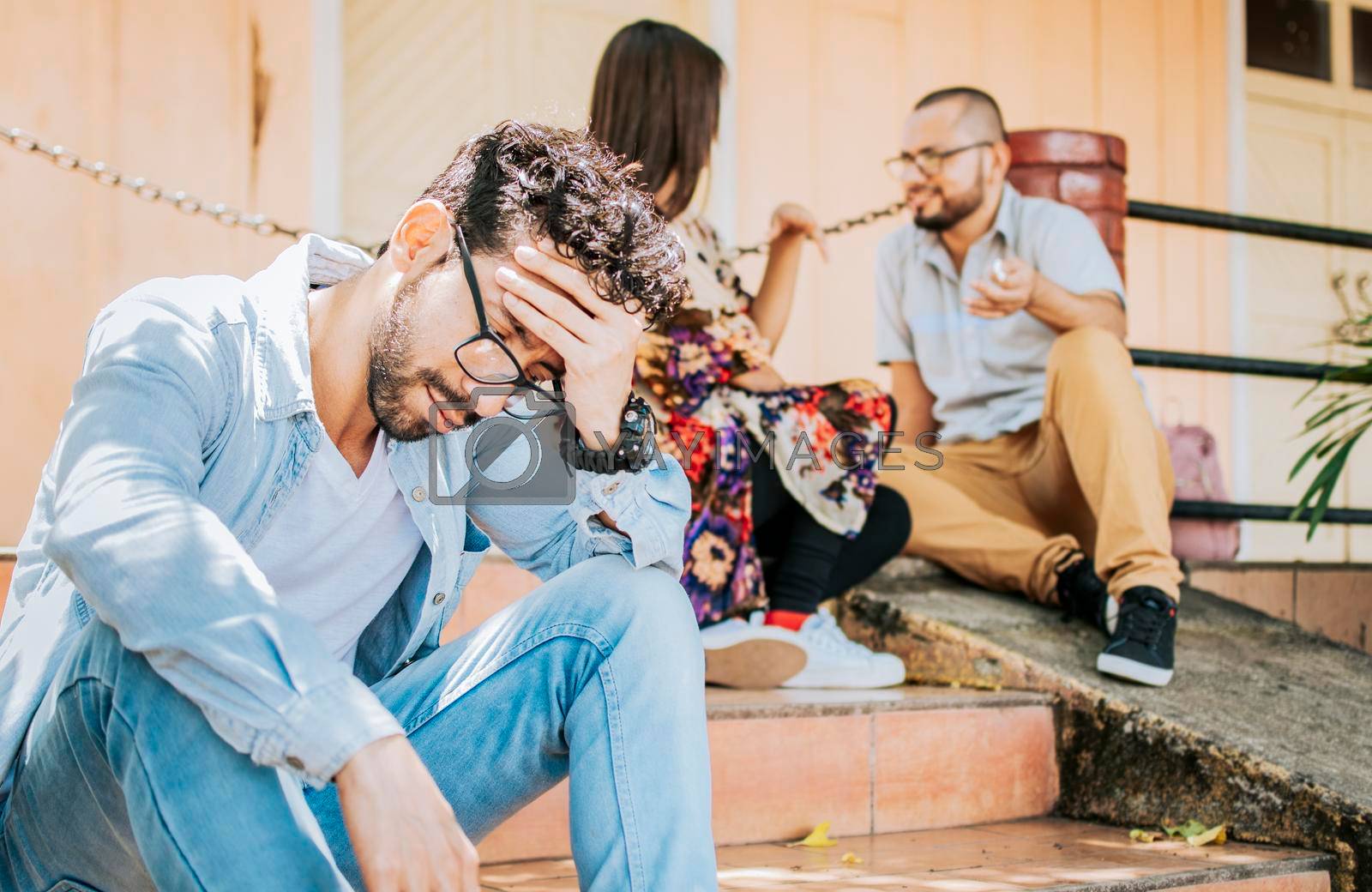Royalty free image of Sad man seeing his girlfriend cheating with his friend. Sad boyfriend sitting on some stairs while his girlfriend talking to another man. Girl talking to another man and her boyfriend is offended by isaiphoto