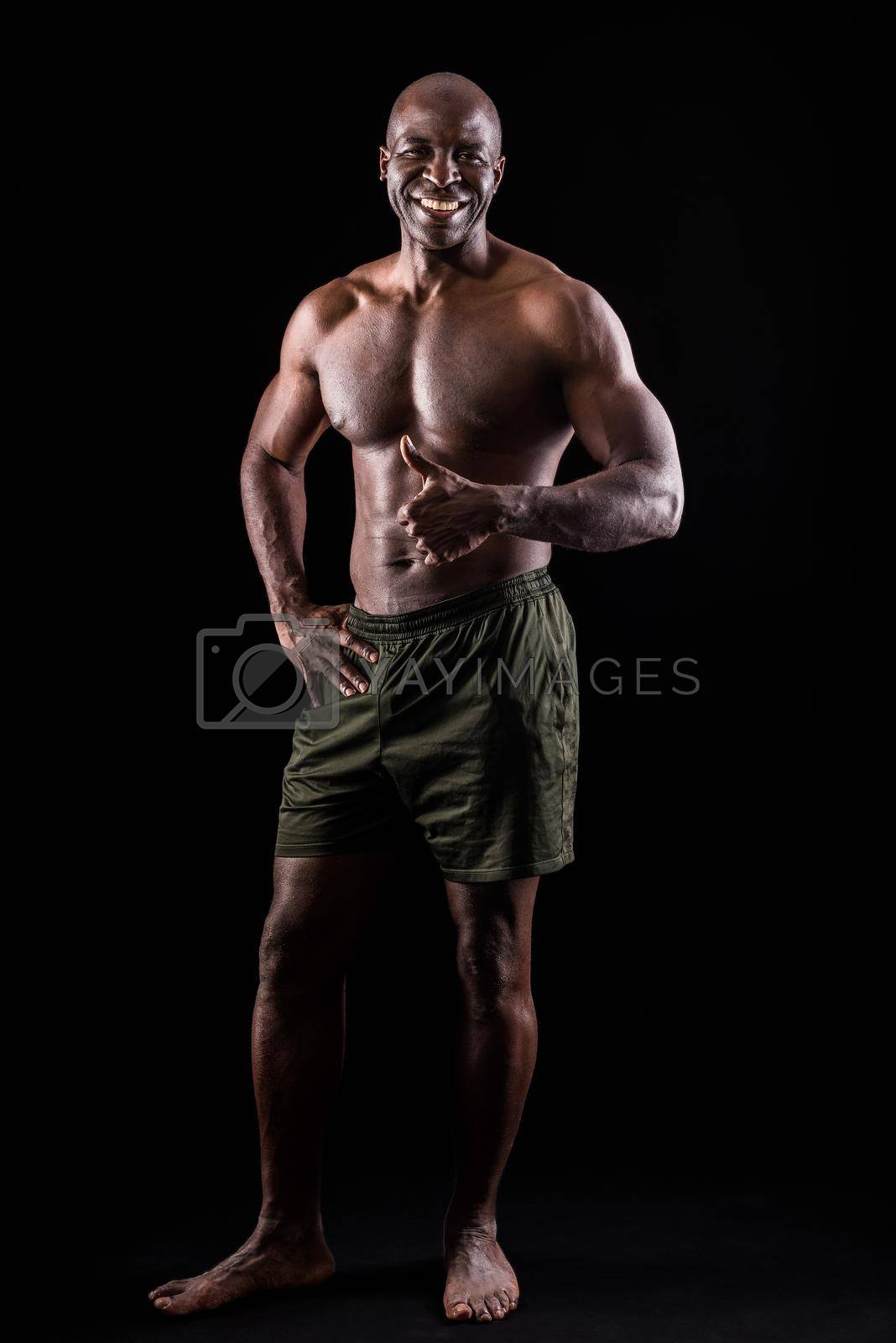 Royalty free image of Cheerful adult muscular man standing looking at camera with a hand on waist and doing thumbs up with the other hand by ivanmoreno